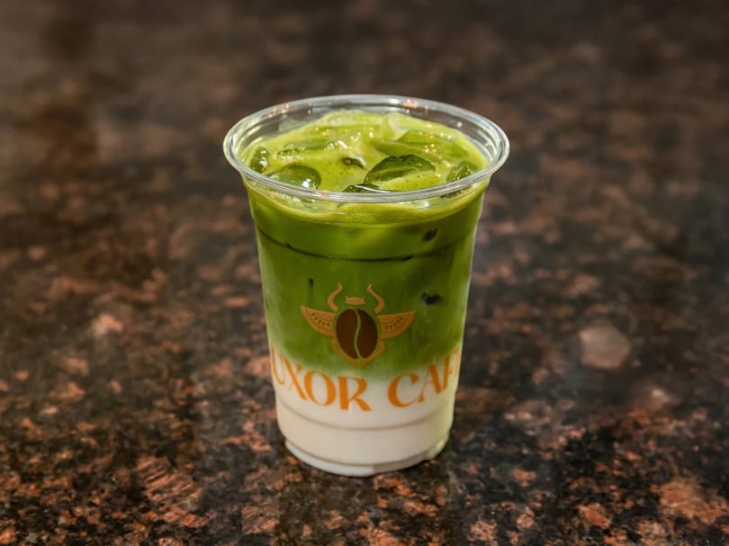 Iced matcha latte with a Luxor Cafe logo on a dark speckled counter.