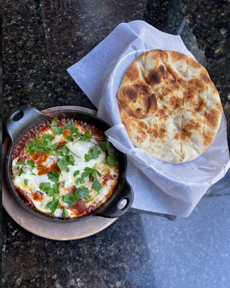 Shakshuka in a cast iron skillet with fresh parsley, served with warm pita bread.
